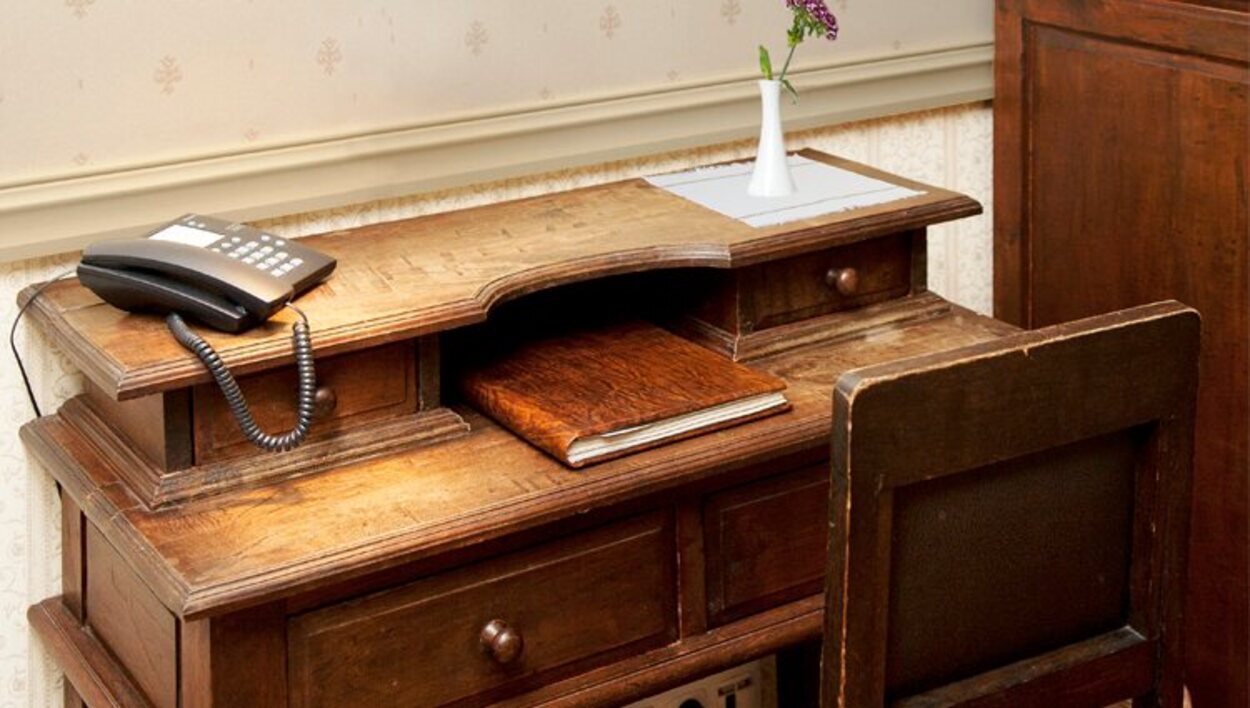 Un antiguo y robusto escritorio con un teléfono moderno encima